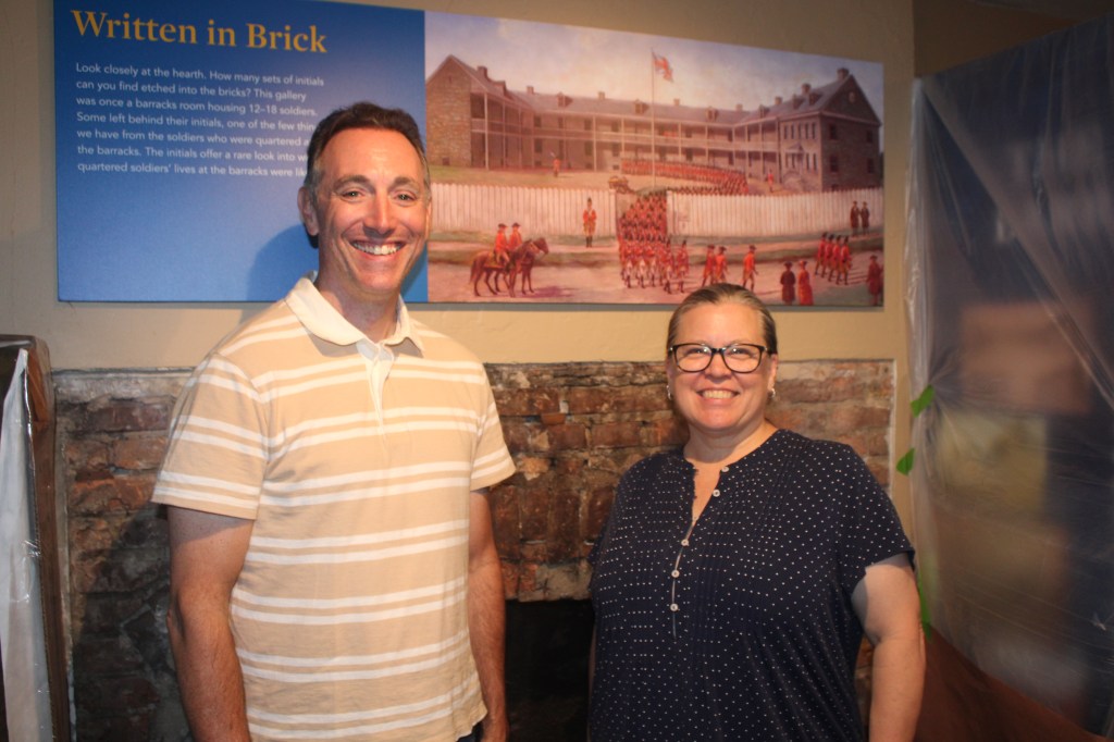 Michele Doherty, executive director for the Old Barracks Museum, and Mark A. Turdo, the Assistant Director of Interpretation and Curation, pose in front of the original 1758 fireplace engraved with the initials of Barrack soldiers. 
Photo credit: Lucy Harper / NJ State House News Service 
